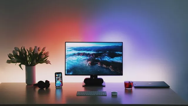 Des appareils high tech posés sur un bureau avec un éclairage d'ambiance rouge/bleu et un pot de fleur